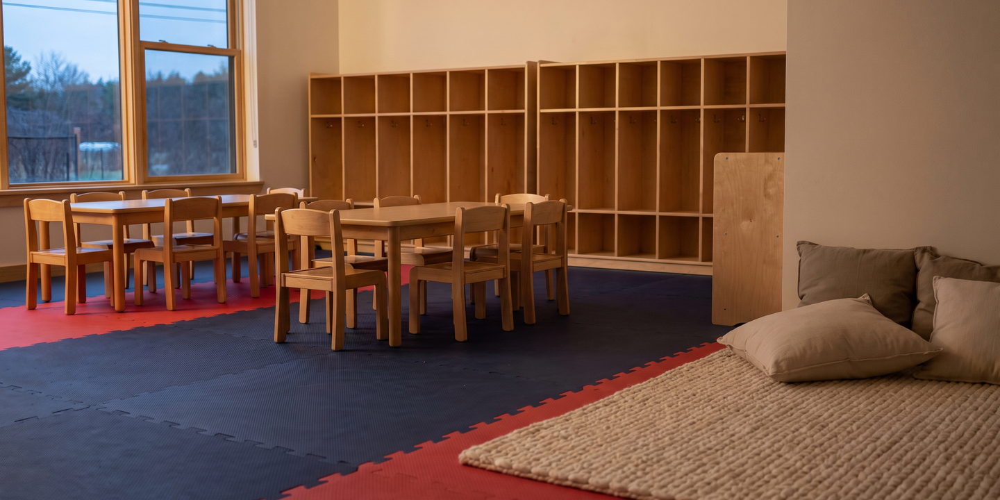 An empty daycare classroom after hours with low tables, small chairs and wall cubbies.